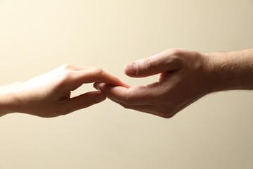 Man and woman holding hands together on beige background, closeup - obrazy, fototapety, plakaty