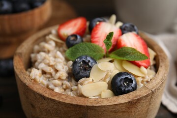 Tasty oatmeal with strawberries, blueberries and almond petals in bowl on table, closeup
