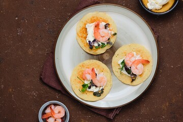 Pancakes with cream cheese, microseneous and shrimp on a ceramic plate on a brown concrete background. Pancakes recipes, snacks. International Pancake Day.