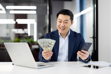 Businessman holding money and smartphone in office