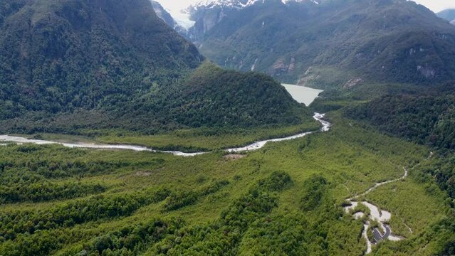 The camera pans up from the green forest to the glacier with waterfall and lake at Queulat National Park in Patagonia Chile snow-capped mountains and river