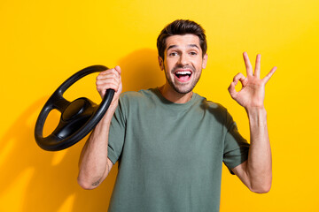 Portrait of overjoyed nice guy with stubble holding steering wheel showign okey approve service isolated on yellow color background