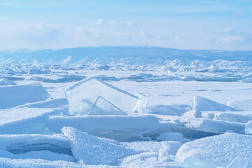 Ice hummocks against blue sky and mountains on Baikal Lake. Transparent blue ice floe. Great backdrop for your design with copy space.