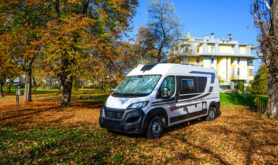Camper van or motor home is parked in city camping under the trees in autumn. Motorhome resting in empty camping in Sarajevo, Bosnia. Campervan and autumn leaves. 