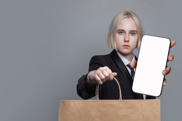 Fototapeta na wymiar Blonde woman with smartphone and shopping bag on gray background