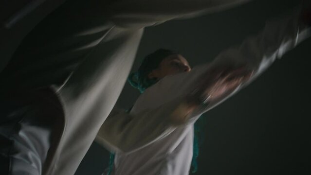 Low angle footage of male fencing instructor teaching novice swordswoman using rapier and making jabs in dark room. Making success during training