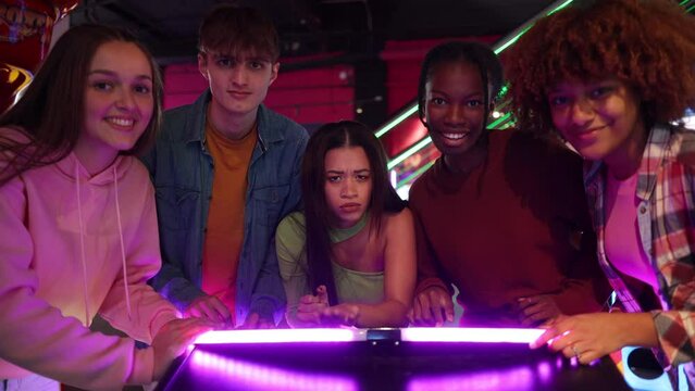 Front view of group multiethnic friends playing arcade games celebrating victory by high-fiving hands