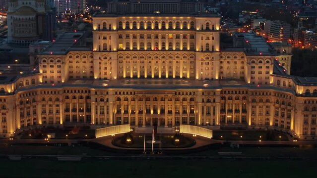 Aerial drone view of illuminated Palace of the Parliament in Bucharest downtown in the evening. Multiple districts around. Romania