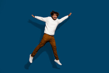 Full length photo of funky excited guy dressed white pullover jumping high empty space isolated dark blue color background