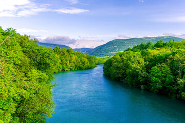 Fototapeta na wymiar beautiful landscape of spring or summer sunset river with blue water and green hills on sides and mountains with amazing cloude sky on background