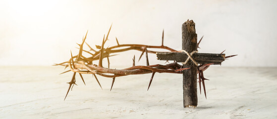 Wooden cross with crown of thorns on light background. Good Friday concept