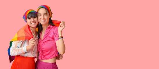 Young lesbian couple with LGBT flag on pink background with space for text