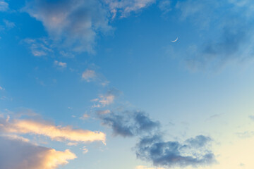 Gently blue sunset sky with pink clouds and moon disk, nature meteorology background