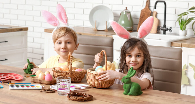 Cute little children with bunny ears and baskets of Easter eggs at home