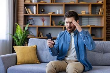Worried man sitting on couch looking at smartphone