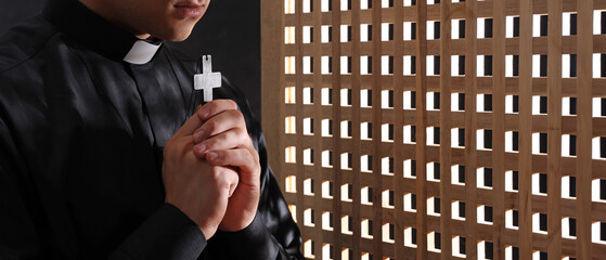 Young priest with cross in confession booth, closeup - obrazy, fototapety, plakaty