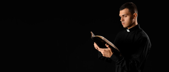 Young priest reading Holy Bible on dark background