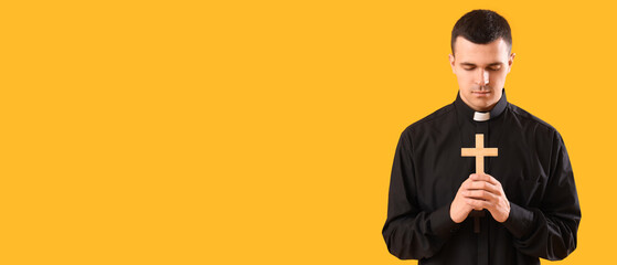 Young priest with cross on yellow background