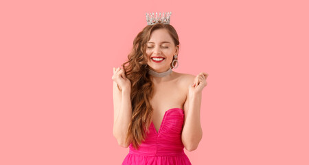 Happy young woman in crown and bright prom dress on pink background