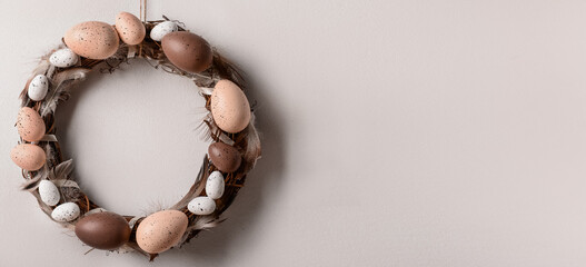 Easter wreath made of eggs and feathers hanging on white wall