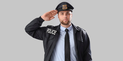Male police officer saluting on grey background
