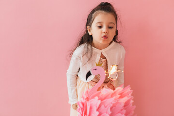 Adorable little girl in a pink dress posing next to a flamingo birthday cake and celebrating her...