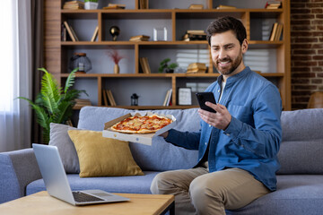 Smiling man enjoying pizza while using smartphone at home
