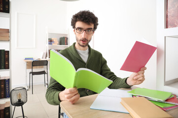 Shocked male student studying with copybooks at table in library