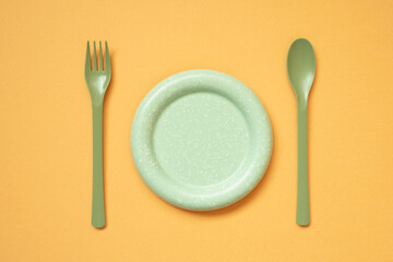 Empty green plate and cutlery on orange table background. flat lay, top view
