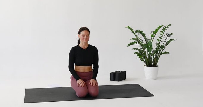 Athletic woman performs Kapalbhati exercise for respiratory tract, clears lungs and sinuses, practices yoga while sitting on mat in bright room