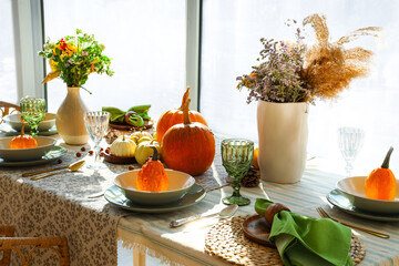 Autumn setting with pumpkins and flowers on dining table in room