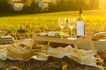 Picnic with tasty food and wine in field at sunset