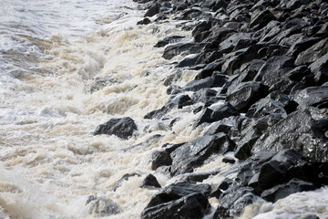 Waves crash on granite stones during a storm on the Black Sea coast. City embankment on a cloudy winter day in Odessa