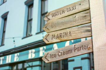 Obraz premium Beach and holiday concept image. A wooden signpost points to various seaside attractions. Tourism and information picture. Water taxi, Ice cream, Deli and Marina wording. Blue.
