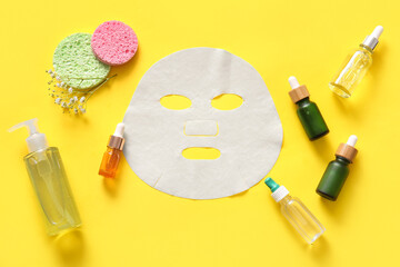 Facial sheet mask with different cosmetic products and gypsophila flowers on yellow background