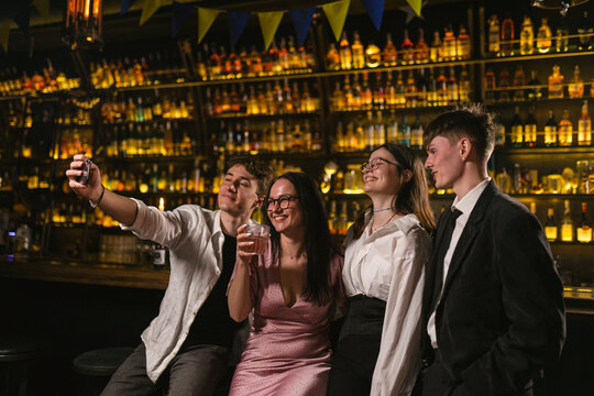 Cheerful company rests after hard week in contemporary pub. Selfie after noisy party with alcoholic cocktails in trendy place