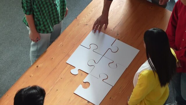 Top view of skilled business people gathering jigsaw piece together.Startup team with casual cloth standing at table while put jigsaw on table. Show unity, cooperation and team working. Convocation.