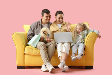 Happy family with dog shopping online on sofa against pink background