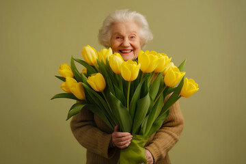 Elderly Woman with Yellow Tulips on olive isolated background. Joyous senior lady smiles brightly as she holds large bouquet of vibrant yellow tulips, conveying warmth happiness. Beautiful grandmother