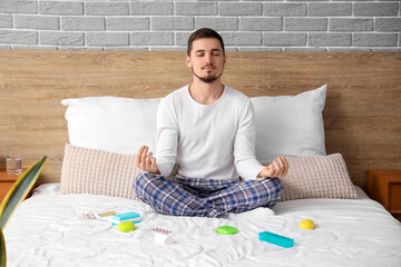 Young man with different pills meditating before sleep in bedroom