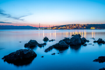 Panoramic night view of the city of Rijeka with many light in refinery in foreground. Croatia.