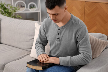 Young man with Bible praying in living room