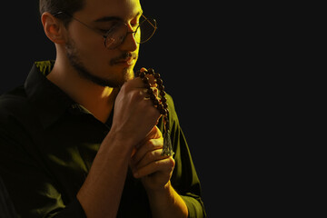 Young man with rosary beads praying on black background