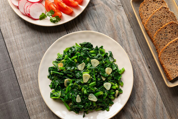 Colorful vegan meal. Stir-fried spinach leaves with garlic, plate with slices of homemade rye bread, and  plate with fresh-cut vegetables.