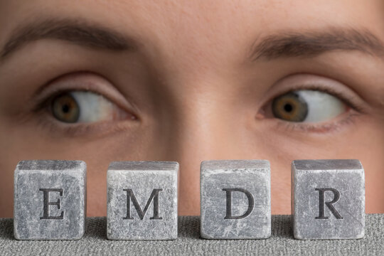 Eye Movement Desensitization and Reprocessing psychotherapy treatment concept. Letters EMDR written on grey stone cubes blocks. Close-up woman's face with eyes looking right. 