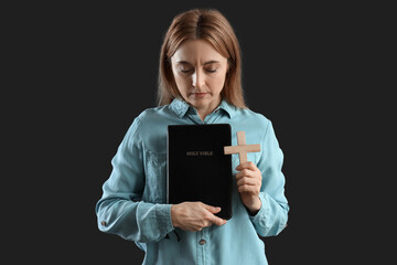 Mature woman with Holy Bible praying on dark background