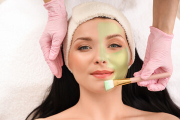 Young woman receiving facial mask in beauty salon, closeup