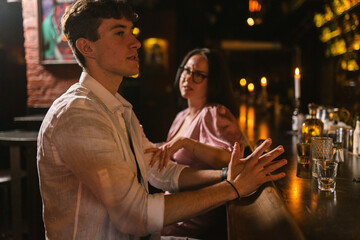 Young man waits for ordered drinks and woman touches arm in bar. Lady pays attention of boyfriend at night party in club