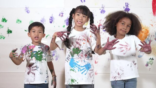 Diverse students put hand up together show colorful stained hands. Group of learner standing in front white background with stained hands while looking at camera. Creative activity concept. Erudition.
