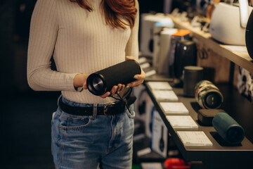 a woman in an electronics store buys a portable audio speaker